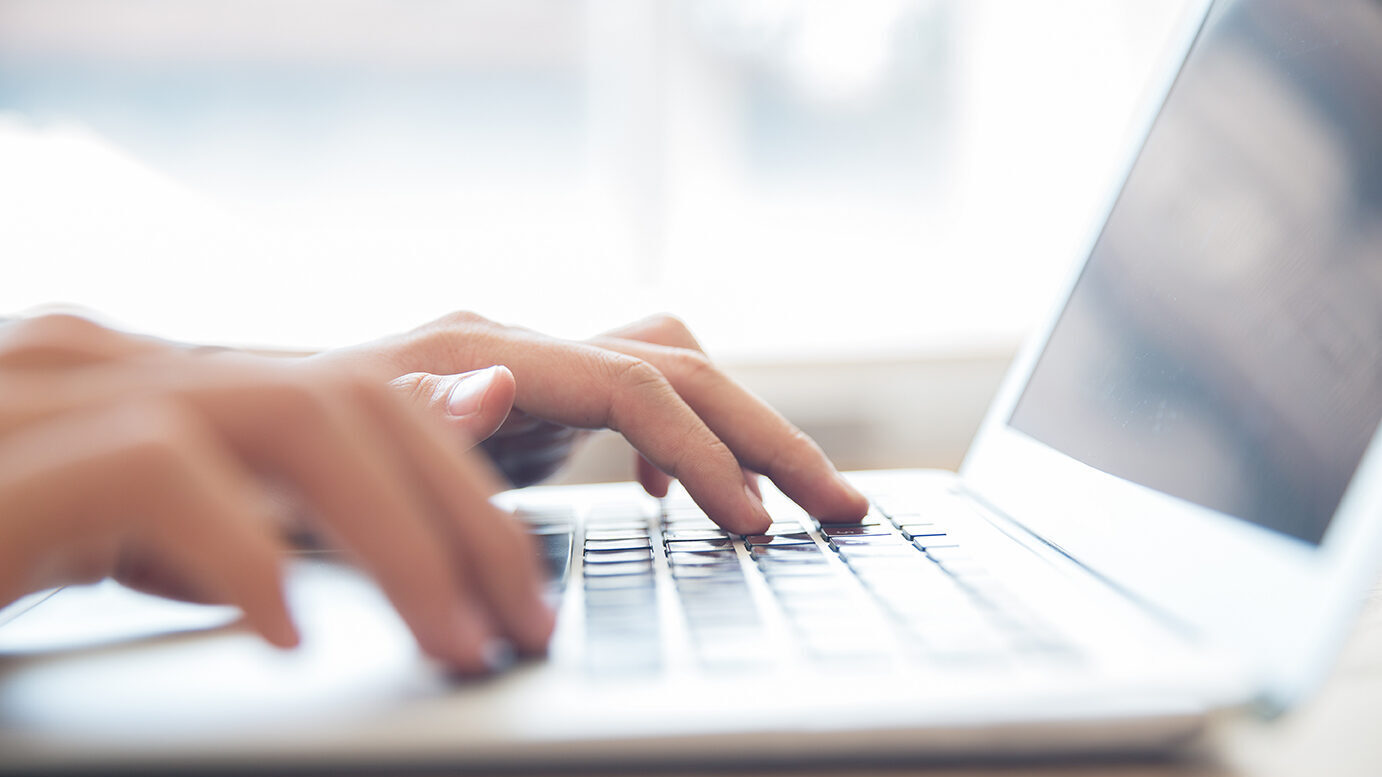 Close-up of hands typing on laptop keyboard indoors.