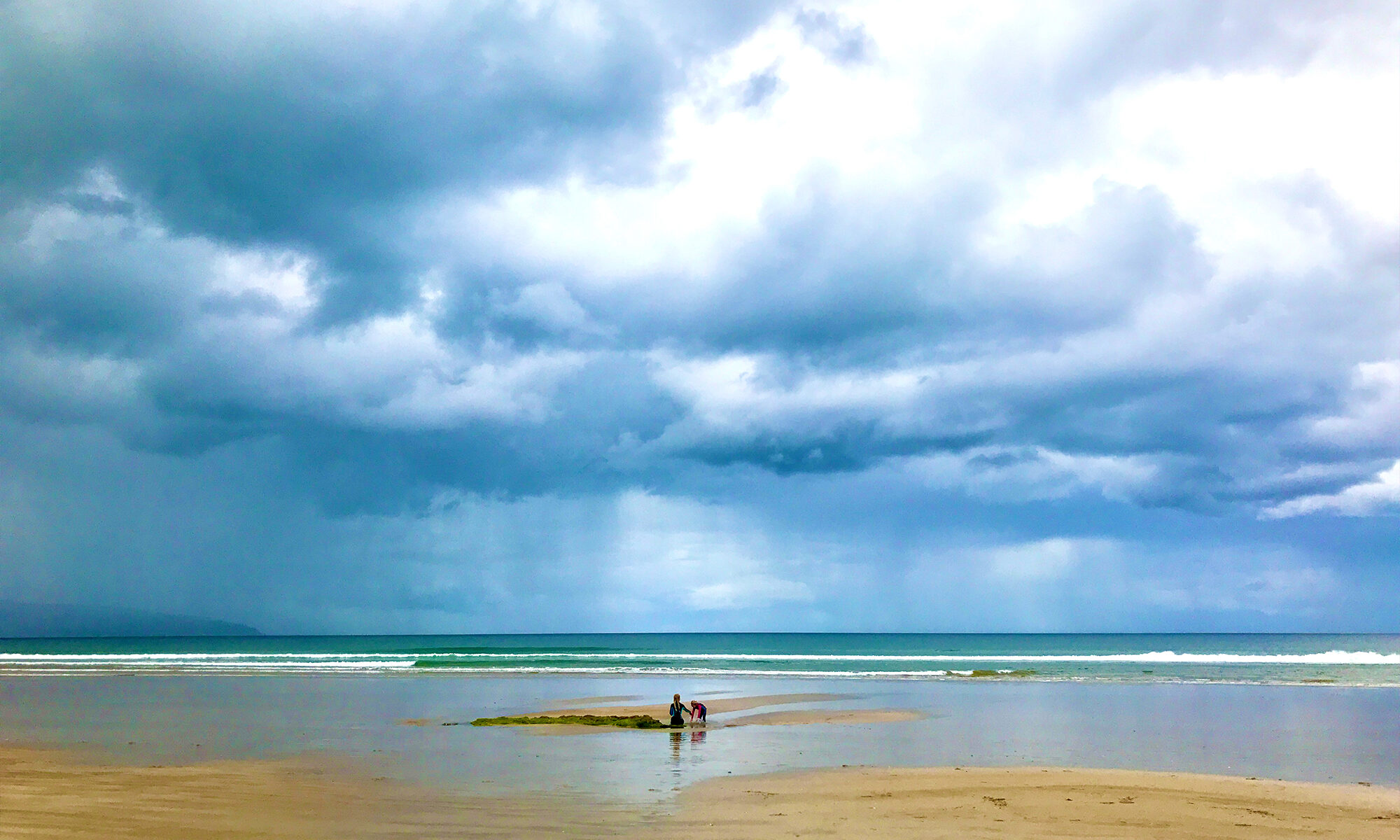 Stormy Beach scene looking out to sea with two small figures playing on the beach